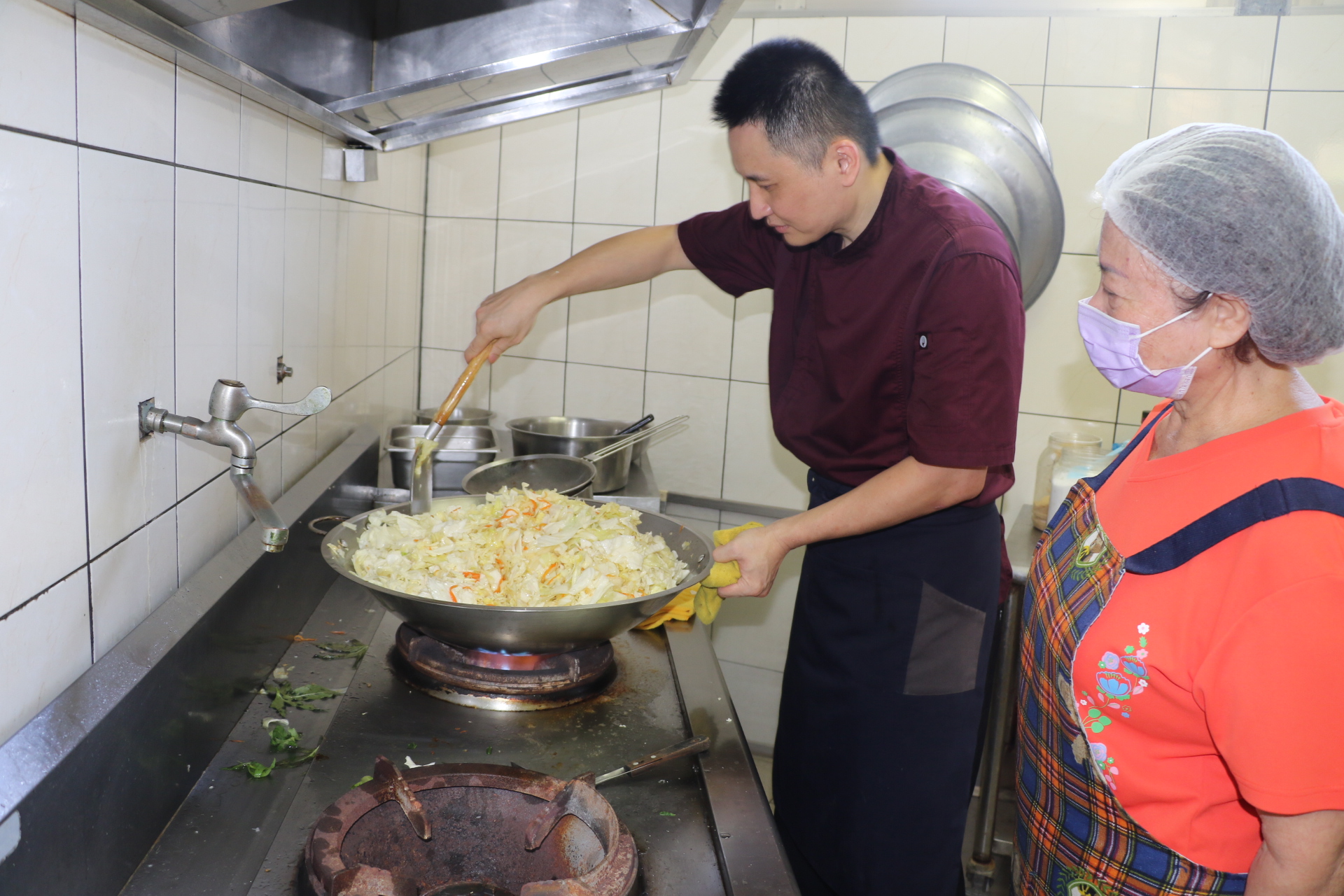 五星級飯店主廚的陳佳瑋專程到新莊牡丹心社區發展協會照顧關懷據點為長輩義煮 志工在一旁討教